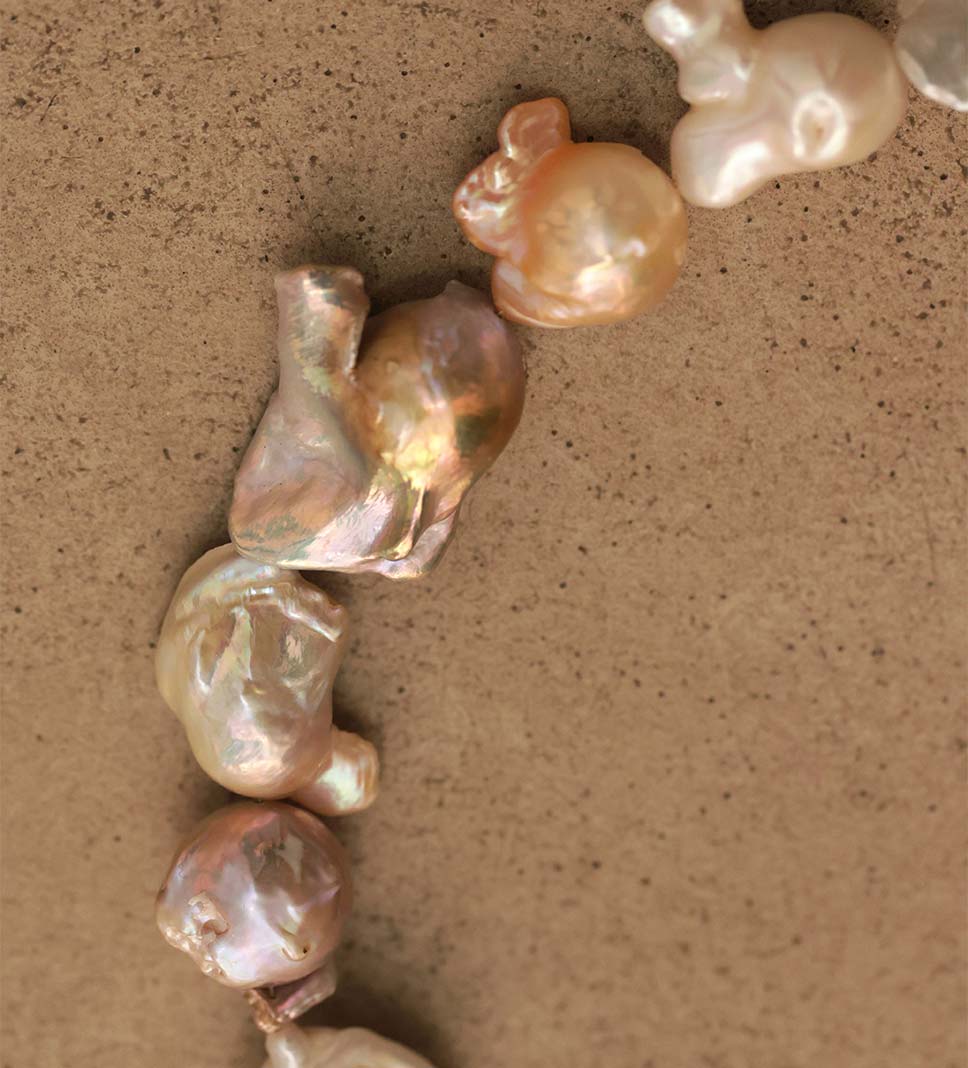 Gros plan sur un collier de perles baroques XL aux formes spectaculairement irrégulières, présentant des teintes nacrées multicolores allant du doré au rose, en passant par le blanc, assemblé à Paris.